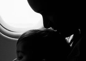 Silhouette of a mother and child gazing out an airplane window during flight.